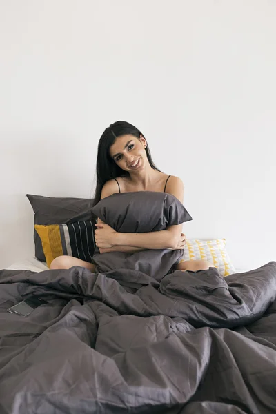 Lachende mooi meisje kussen omhelzen zittend op bed in de ochtend — Stockfoto