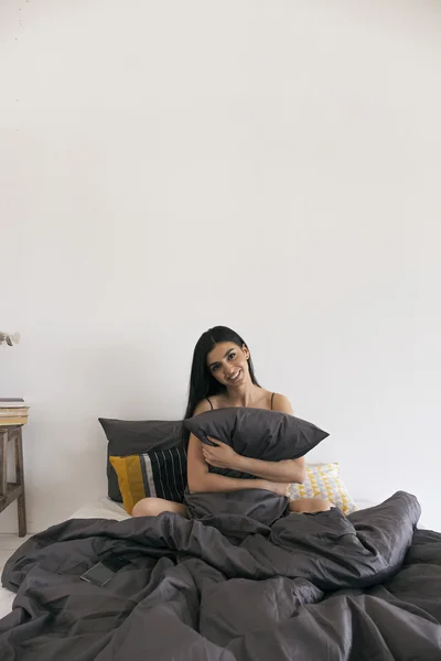 Menina sorridente bonita na cama abraçando travesseiro — Fotografia de Stock