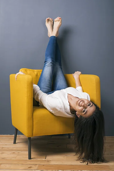 Босонога усміхнена дівчина на стільці з ногами, схрещеними на стіні Ліцензійні Стокові Фото