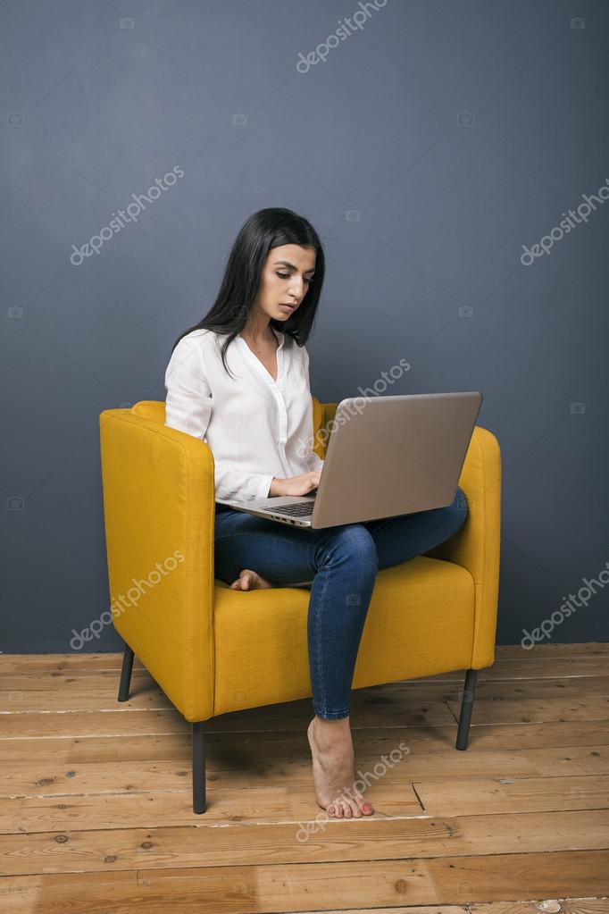 Barfüßige junge Frau arbeitet zu Hause am Laptop ...
