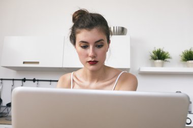 Esmer freelancer mutfakta otururken dizüstü bilgisayarda bakıyor