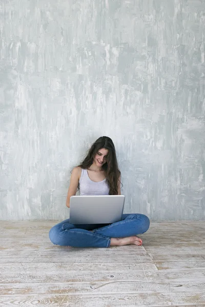 Barefoot woman smiling at laptop while sitting on floor with crossed legs — Stock Photo, Image
