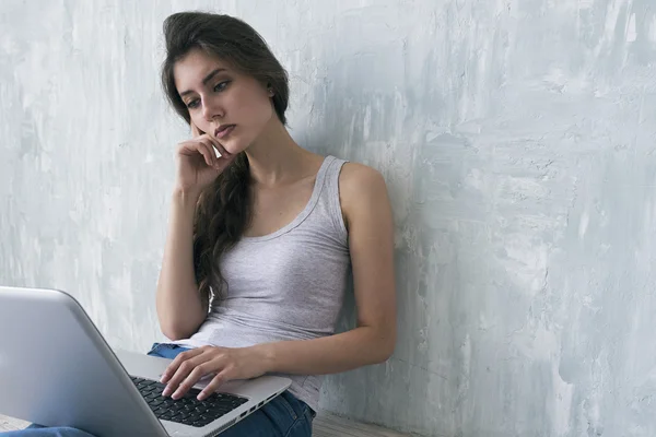 Serious brunette using laptop and leaning on cement wall — Stock Photo, Image