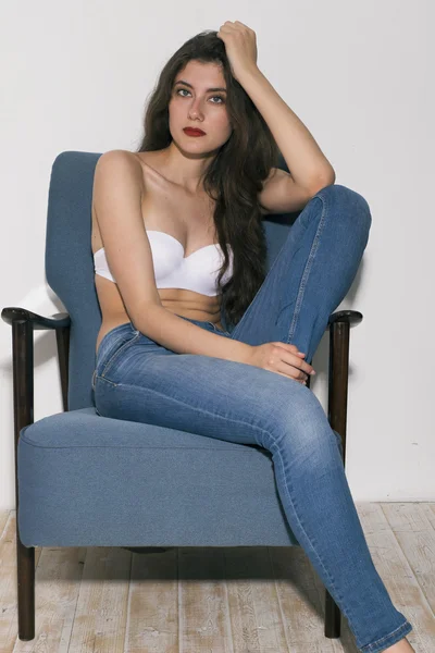 Girl in white bra and jeans on arm-chair — Stock Photo, Image