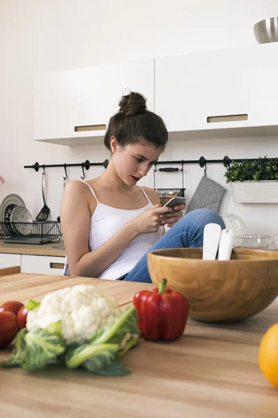 Портрет молодой женщины с помощью телефона за столом с овощами — стоковое фото