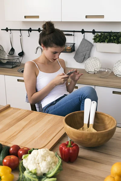 Calma morena mensajes de texto sobre la celda mientras está sentado en la cocina — Foto de Stock