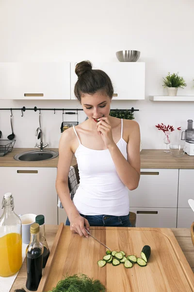 Retrato de morena comiendo pepino cortado mientras cocina —  Fotos de Stock