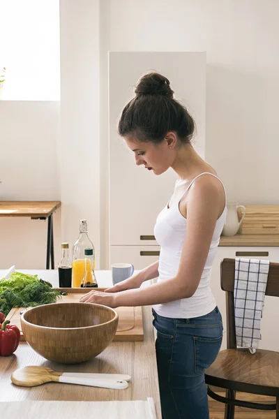 Vue latérale de la jeune brune préparant une salade en cuisine — Photo