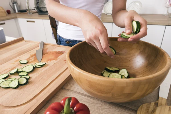 Gros plan de la femme qui met du concombre coupé dans un bol — Photo