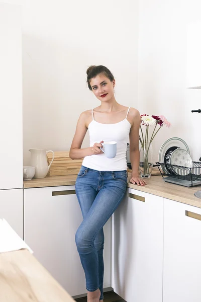 Linda morena com lábios vermelhos segurando xícara de café na cozinha — Fotografia de Stock