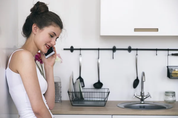 Widok z boku kobiety, rozmawiając przez komórkę w kuchni — Zdjęcie stockowe