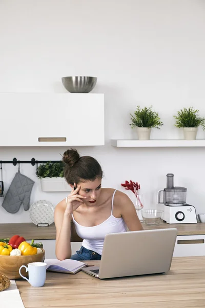 Mujer pensativa trabajando en el ordenador portátil en la cocina —  Fotos de Stock