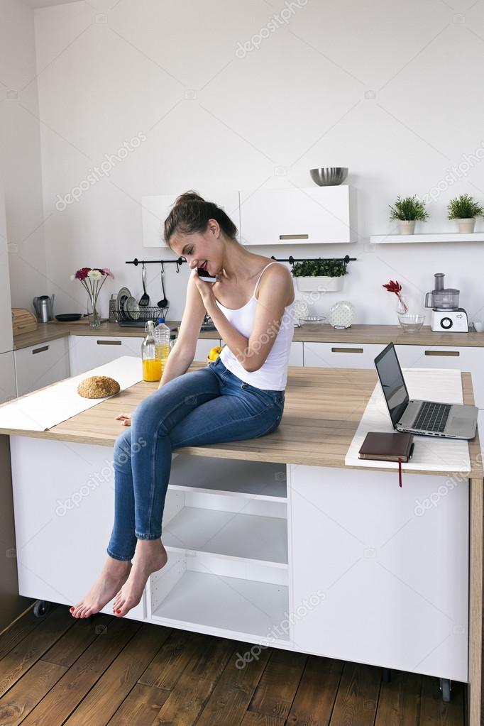 Mujer con las piernas cruzadas sobre la mesa de la cocina hablando ... Mujer con las piernas cruzadas sobre la mesa de la cocina hablando ...