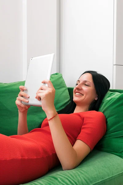 Sonriendo hermosa mujer usando la tableta en el sofá —  Fotos de Stock