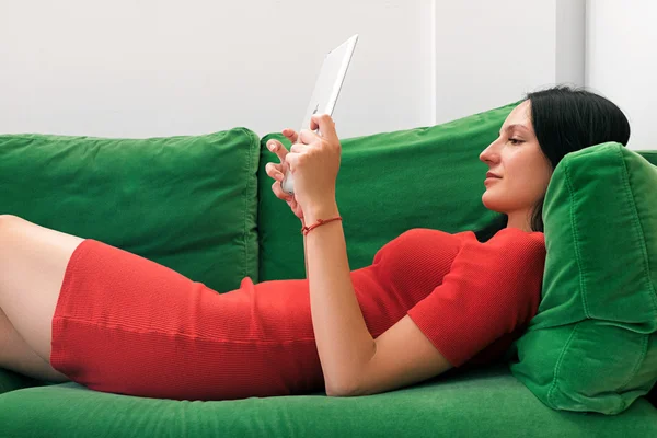 Uśmiechnięta kobieta za pomocą tabletu leżąc na kanapie — Zdjęcie stockowe