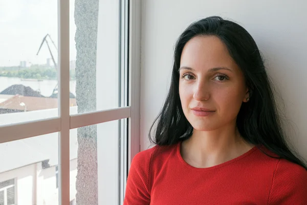 Bella donna dai capelli neri in rosso vicino alla finestra — Foto Stock