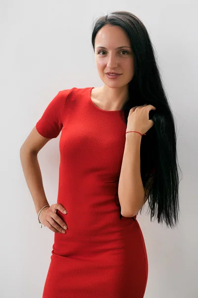Елегантна жінка в червоній сукні з довгим чорним волоссям посміхається на камеру Ліцензійні Стокові Зображення