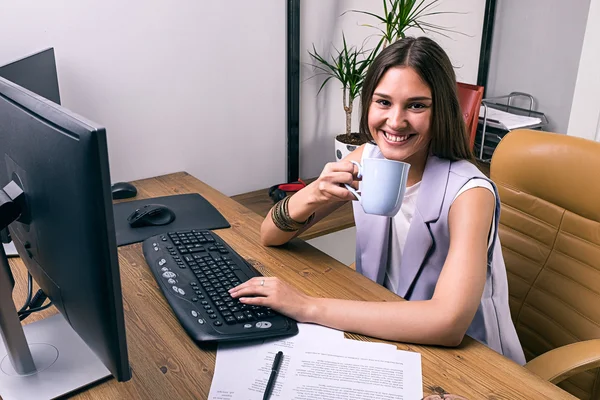 Bruna sorridente con bevanda che lavora al computer — Foto Stock