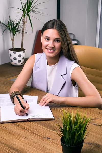 Vacker ung affärskvinna tittar på kameran medan du tar anteckningar i office — Stockfoto