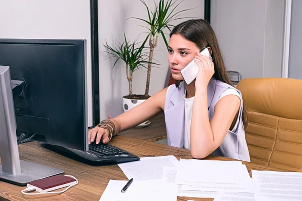 Empresaria usando teléfono inteligente mientras trabaja en la computadora — Foto de Stock