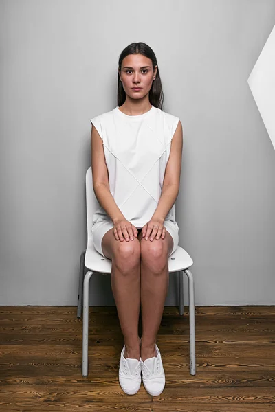 Retrato de menina em vestido branco na cadeira com as mãos nos joelhos — Fotografia de Stock