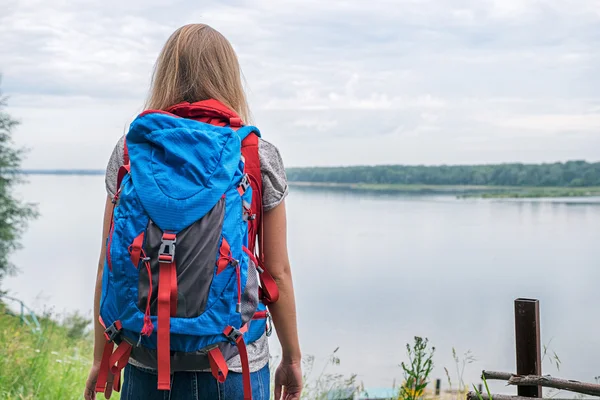 Vista trasera de chica rubia con mochila azul viendo el río —  Fotos de Stock