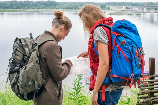 Two female travelers looking down at map at river
