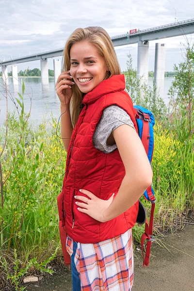 Happy usměvavá batohem v červené vestě, poslechu hudby do sluchátek — Stock fotografie