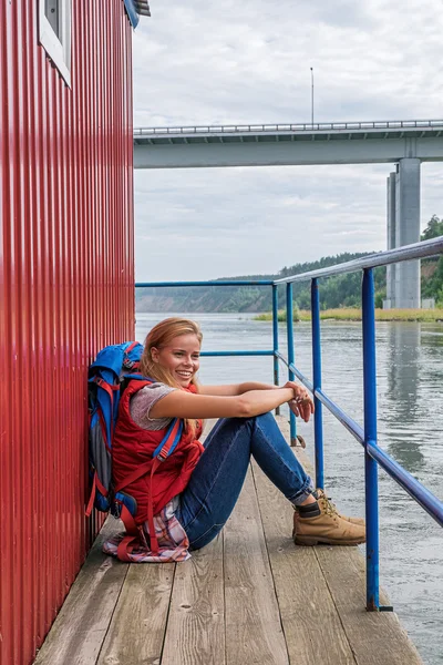 Wesoły backpacker blondynka na molo uśmiechający się od — Zdjęcie stockowe