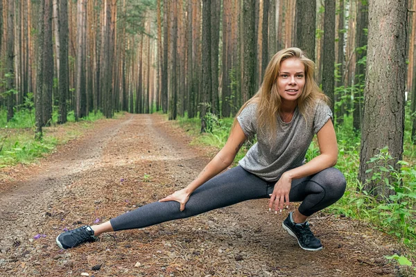 Blonde coureuse s'étirant sur la route forestière — Photo