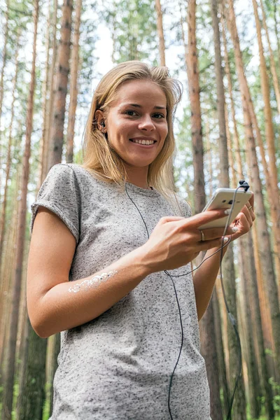 Beautiful smiling girl listening to music using cell in forest — Stock Photo, Image