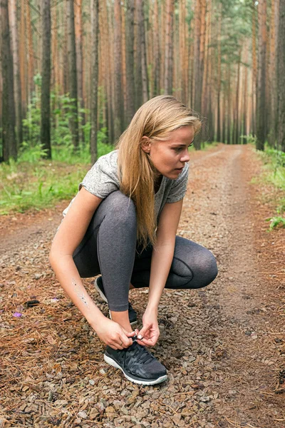 Blonde Athletin bindet Schnürsenkel an Turnschuhe im Wald — Stockfoto
