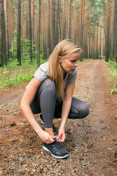 Atleta loira amarrando atacadores em tênis na floresta — Fotografia de Stock