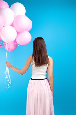 Arkadan görünüş ile mavi arka plan üzerinde birçok pembe hava balon etekle tanınmaz kız. Stüdyo vurdu