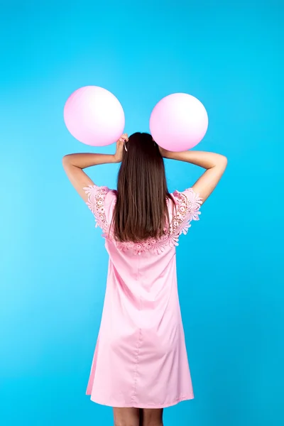 一个工作室拍摄的无法辨认的年轻女孩粉红色的礼服与两个气球在头上 蓝色背景 — 图库照片