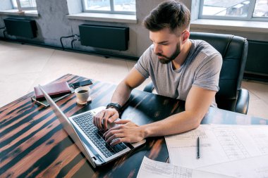 Çizimleri ile masada dizüstü bilgisayar kullanan sakallı adam portresi