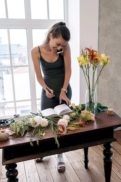 電話で話していると花とテーブルでノートに書いて幸せと忙しい花屋の肖像画 — ストック写真