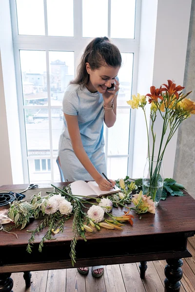 Retrato Florista Feliz Escribiendo Cuaderno Mientras Habla Móvil Mesa Con — Foto de Stock