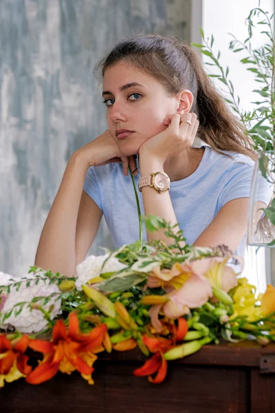 ब्रुनेट लड़की का चित्र कैमरा को देखते हुए फूलों के साथ टेबल पर बैठे हुए रॉयल्टी फ़्री स्टॉक फ़ोटो