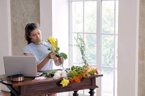 Jonge Brunette Houdt Verschillende Verse Bloemen Boven Tafel Met Laptop Stockafbeelding