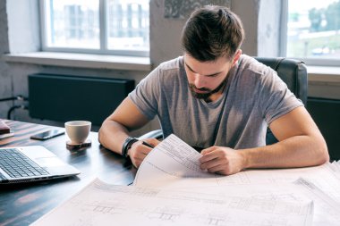 Ofisteki çizimleri analiz etmekle meşgul genç bir mimar.