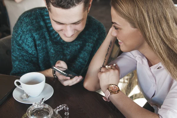 Young couple surfing the web looking at photos on mobile phone. In a cafe. — Stock Photo, Image