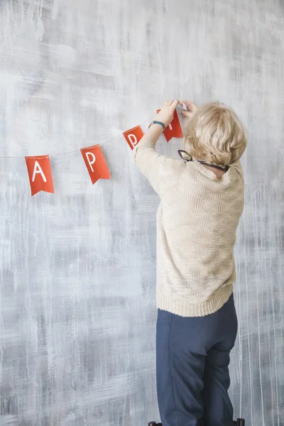 Elderly woman decorating the wall with handmade garland — Stock Photo, Image