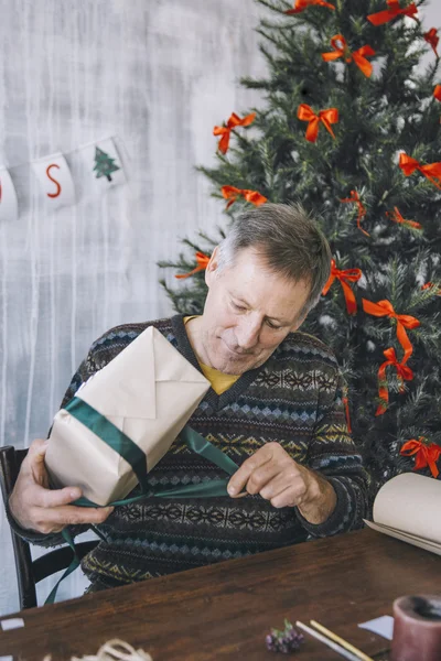 Elderly man decorating the Christmas present — Stock Photo, Image