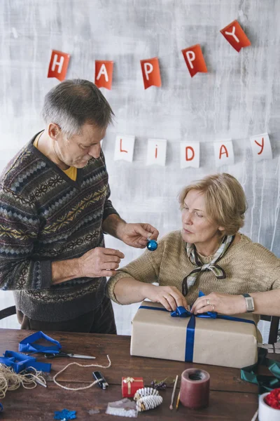 Пожилая пара украшает рождественский подарок голубой лентой — стоковое фото