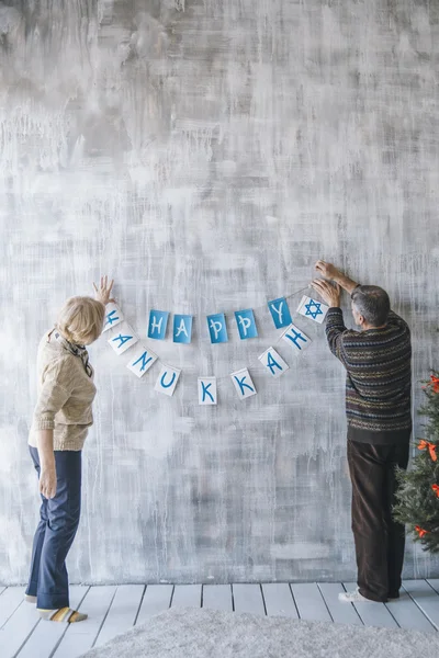 Dos personas mayores decorando la casa con guirnaldas de Navidad — Foto de Stock