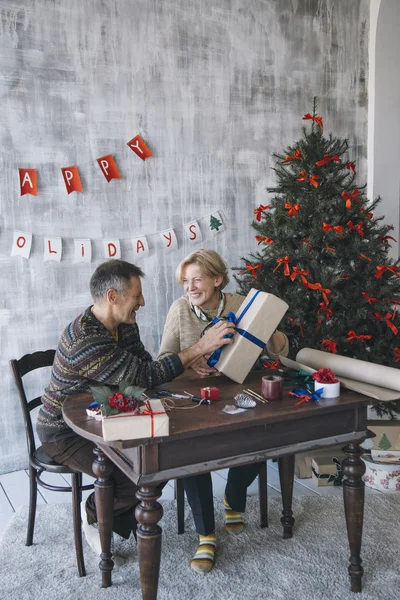 Duas pessoas idosas sorrindo juntas enquanto sentadas na mesa de madeira. Tempo de Natal Imagem De Stock