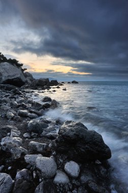 Kayalık sahilde gün doğumu. Alacakaranlıkta dramatik deniz manzarası
