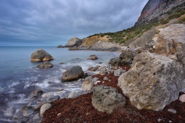 Kayalık sahilde gün doğumu. Alacakaranlıkta dramatik deniz manzarası
