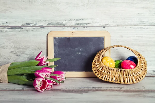 Blackboard with pink tulips and basket with eggs — Stock Photo, Image